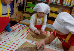 Dwoje dzieci podczas wykrawania foremkami pierniczków z rozwałkowanego ciasta.